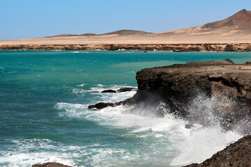 The Atlantic Ocean in Jandia with clear sky and mountains in the back and waves breaking on the...