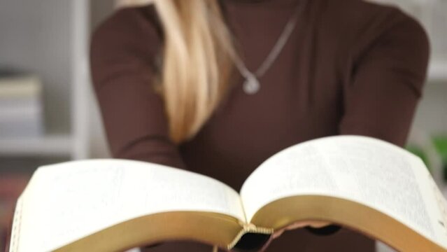 A woman's hand holds a book. A mysterious book opening. Story of the book. Selective focus on paperback. Female holding bible in hands. Opening of Holy Bible, closeup