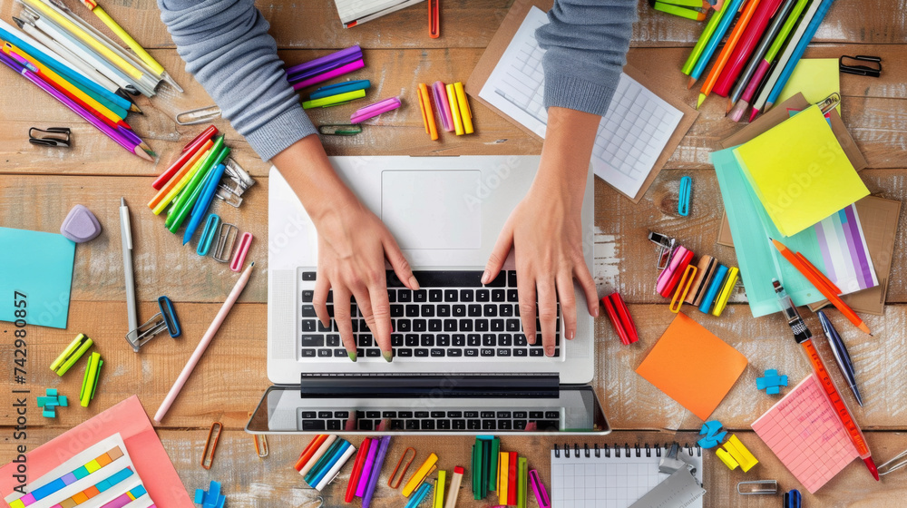 Poster top view of a workspace with hands typing on a laptop keyboard, surrounded by colorful stationery