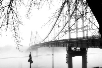 The bridge stands as a solitary sentinel, its arches disappearing into the swirling haze, symbolizing a connection amidst the obscurity.