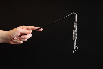 Hand holds a decorative whip with metal balls on a dark background. Sex accessory in a woman's...