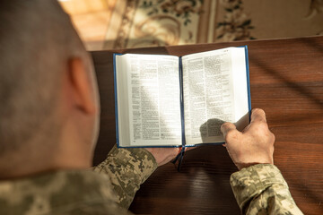 Lifestyle portrait of Soldier in uniform reading Holy Bible. Natural aesthetic light