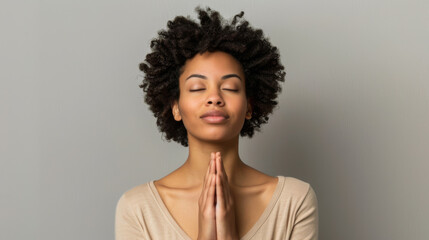 A serene individual with closed eyes is meditating, hands clasped together in a gesture of peace against a neutral background. - obrazy, fototapety, plakaty