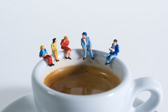 Photography of miniature people and toy figures, a group of people sits on a coffee cup for a break, close up
​