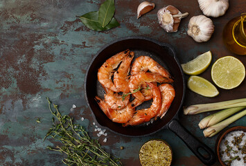 Grilled shrimps in cast iron pan with lime, lemongrass, thyme, garlic, oil and salt over dark green...