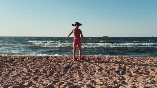 Relaxing by the sea. Shell beach. Footprints on the seawater. A child on the beach of the Sea of Azov. A boy jumps into the sea waves from the beach. The delight of a child from a vacation at sea. 4K