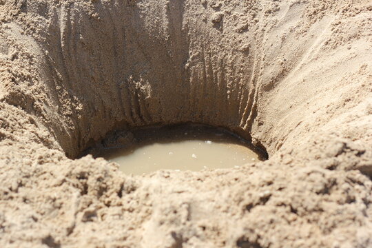 A deep hole dug in the beach sand on a bright sunny summer day.