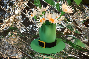 Green leprechaun hat with white flowers on silver background.
