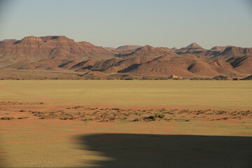 Fototapeta na wymiar red desert sand plaine with bright green fresh grass growing, red mountain range in the background