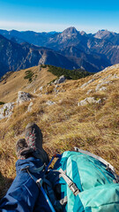 Fototapeta premium Legs of hiker woman resting in alpine meadow with panoramic view of majestic mountain peaks of Gesäuse seen from Hochblaser in Eisenerz, Ennstal Alps, Styria, Austria. Wanderlust concept in summer.