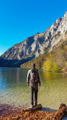 Hiker man at lakeshore of Leopoldsteiner lake in Eisenerz, Ennstal Alps, Styria, Austria. Beautiful reflection on calm water surface of surrounding majestic mountain peaks Austrian Alps. Tranquility