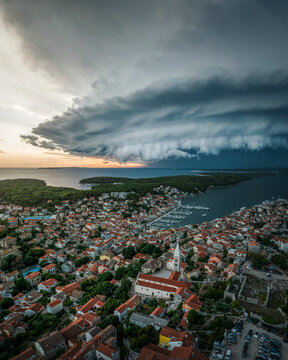 Aerial view of a menacing Supercell storm over a coastal town with red roofs and a church steeple, Mali Losinj, Primorje-Gorski Kotar, Croatia.