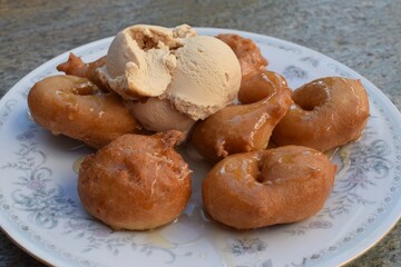 Traditional Greek hot loukoumades at a Greek bakery on Skiathos island in summer. Plate of delicious fresh fried donuts soaked in sweet honey syrup, with a scoop of refreshing ice cream.