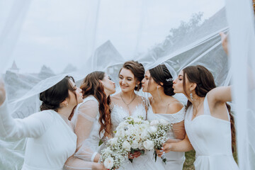Wedding photography in nature. A brunette bride and her girlfriends pose under a veil, holding...