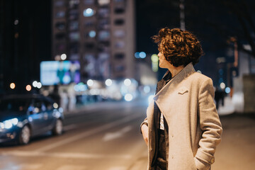 An adult woman in a stylish coat takes in the nightlife, with blurred city lights creating a...
