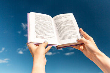 reading, education and knowledge concept - close up of hands holding open book over blue sky