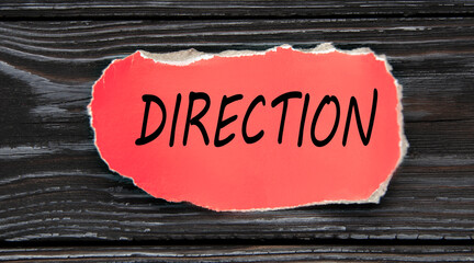 DIRECTION - word on a red torn piece of paper on a dark wooden background