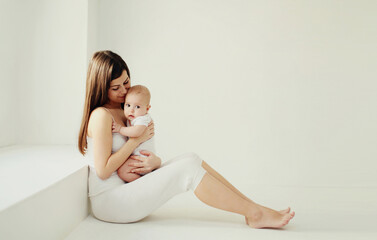 Obraz premium Happy young mother holding cute baby together in white room at home