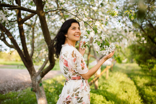 A lovely and beautiful woman enjoys a moment of relaxation in a spring garden adorned with white flowers on a beautiful spring day. A girl smiling with her teeth.