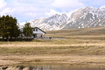 baita o casa di montagna durante l'inverno con cime delle montagne innevate sullo sfondo e lago...