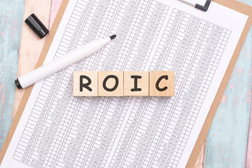 ROIC - inscription on wooden cubes on a white background along with a tabular document. finance and business concept