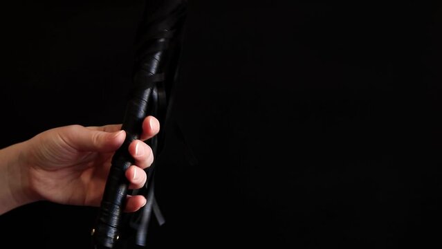A woman's hand holds a whip against a dark background. Leather whip for spanking isolated on black. Sex toy for intimacy. Sexual slavery