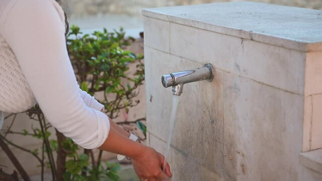 Close-up view of a young woman washing her hands under cold clean water flowing from an urban faucet. Drinking fountain in the city of Quesada in the province of Jaen, Andalusia, Spain