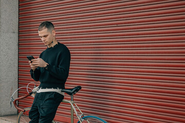 young man with mobile phone and bicycle on the street in red background