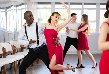Emotional elegant adult African American performing kizomba paired with attractive woman in red,...