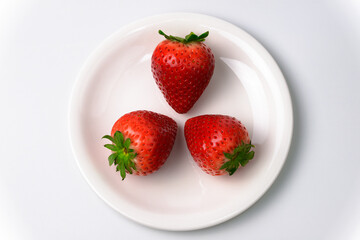 白いお皿に乗った赤く熟した3個の苺