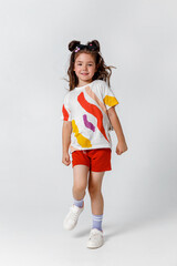 Cute little girl standing in white t-shirt and red shorts on white background. Full length portrait little child girl