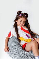 Cute little kid girl in white t-shirt and red shorts sitting on white studio background.