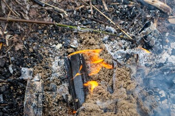 A fire burns in a campfire with a red fire in the background.