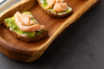 toast with cream cheese, avocado and salmon on a wooden plate, dark background
