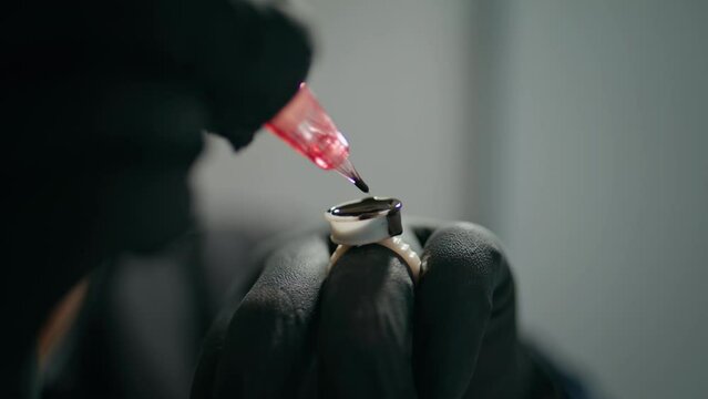 Tattoo needle loading ink in salon closeup. Hands holding permanent paint jar