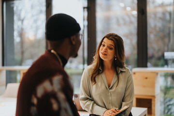 Two diverse professionals in a casual business setting, one holding a tablet, engage in a focused,...