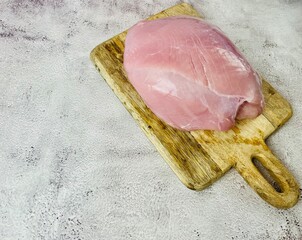 There is a piece of meat from a turkey breast on a gray background on a wooden board. side view ....