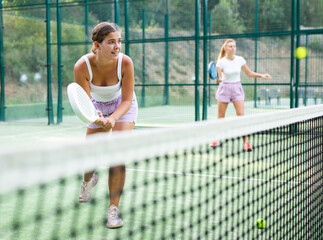 Young woman in shorts playing padel tennis on court. Racket sport training outdoors.