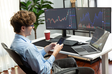 Working young business trader focusing on smartphone comparing with laptop and pc in market stock graph investing in real time screens at home office, analyzing dynamic exchange rate concept. Gusher.