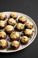 Homemade Garlic Parmesan-Stuffed Mushrooms on a plate on a black background, side view.