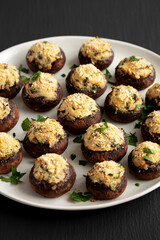 Homemade Garlic Parmesan-Stuffed Mushrooms on a plate on a black background, side view.