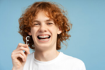Closeup image of smiling teenager with curly red hair and braces, holding an easy flosser