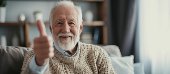 An older man, sitting at home, is joyfully raising his thumb up in approval and positive feedback.