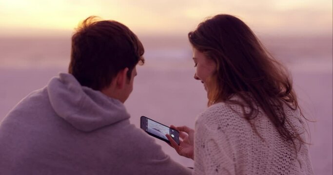 Phone, photography and back of couple at beach on romantic, anniversary or valentines day date. Love, cellphone and young man and woman relax by ocean at sunset for picture on vacation or holiday.