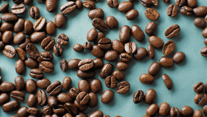 Background of coffee beans on a dark turquoise, cyan background. Coffee beans shift into one pile....