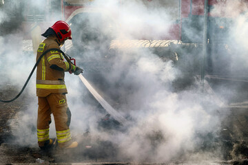 Strażak w kłębach dymu gasi pożar. - obrazy, fototapety, plakaty