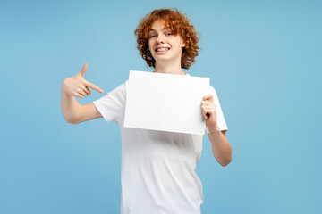 Naklejka premium Good looking redheaded male teen with braces, pointing at a banner, isolated on blue background