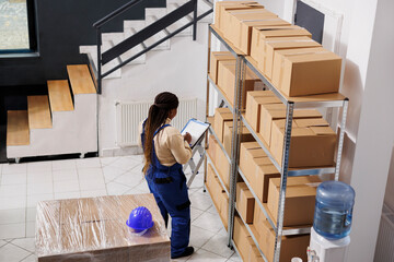 Warehouse manager checking documentation on clipboard and inspecting parcels. African american...
