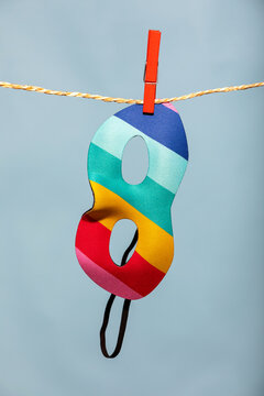Generative AI illustration of colorful striped carnival mask hanging on a clothespin and rope against a light blue background