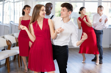 Fototapeta premium Group of young contemporary active people dancing twist or rock and roll dance in dance hall during party